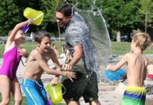Kinder im Garten: So klappt es auch mit den Nachbarn Kinder in Badebekleidung schütten Wasser auf einen Mann in T-Shirt und Shorts