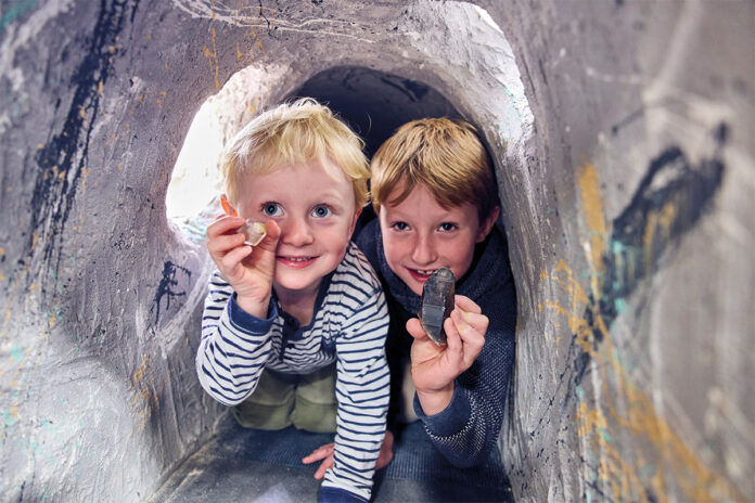 die_munich_show_2025 Zwei Kinder in einer Höhle halten Edelsteine in der Hand