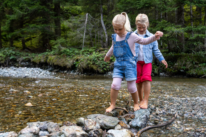 Zwei Kinder balancieren auf einem Baumstamm im Wasser